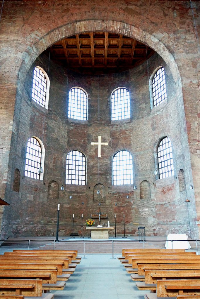 君士坦丁大教堂内部的照片。一个圆形的圆顶结构延伸到一个矩形的房间。照片的右下方和左侧是教堂的长凳，中间是一个小岛。此外，还有一个祭坛和岛的尽头和一个白色的十字架坐在祭坛上面。