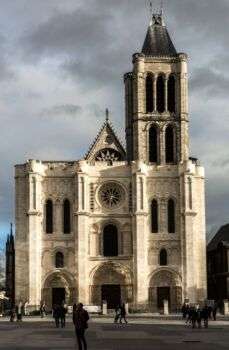 巴黎圣丹尼斯大教堂的照片，这是一个大型的轻石结构，整个建筑的正面都有黑色的拱形窗户。